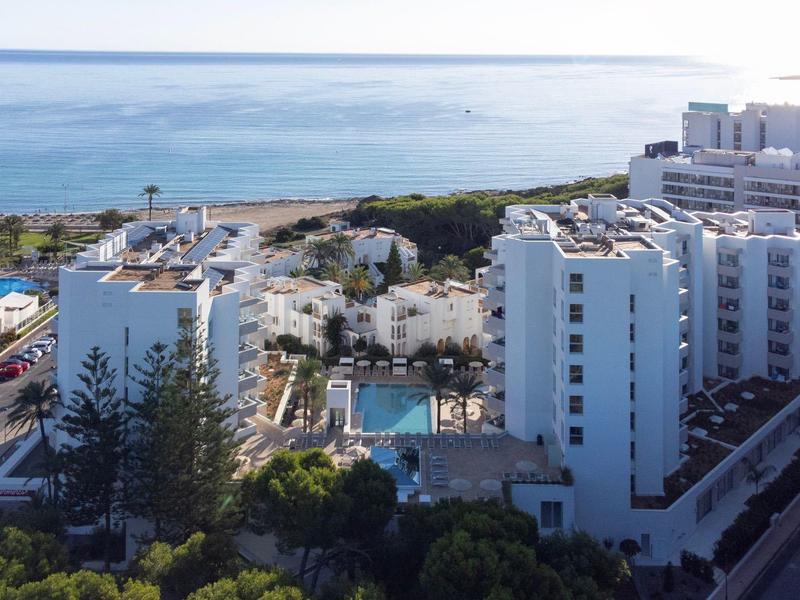 Hotel complex with several buildings and pool, sea in the background during daylight.