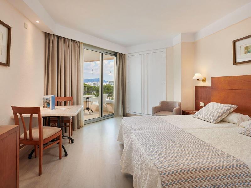 Bright hotel room with two single beds, desk, and balcony access with a view.