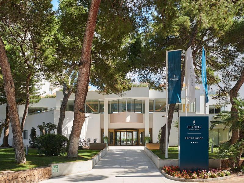 Entrance area of a modern hotel with trees and a path leading to reception.