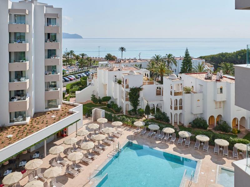 Modern hotel complex with pool, umbrellas, and sea view.