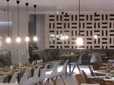 Modernes Restaurant mit hängenden Glühlampen, grauen Stühlen und dekorativer Wandgestaltung.