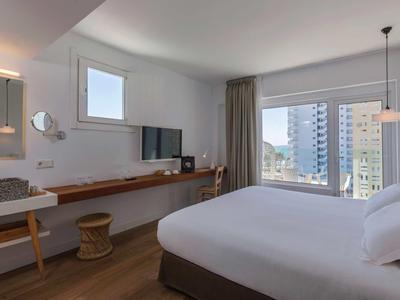 Modernes Hotelzimmer mit großem Bett, Schreibtisch, TV und großer Fensterfront mit Stadtblick.