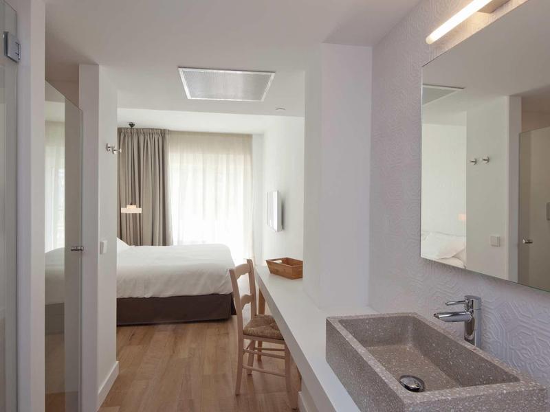 Nowoczesny pokój hotelowy z umywalką, lustrem i widokiem na sypialnię z zasłonami.