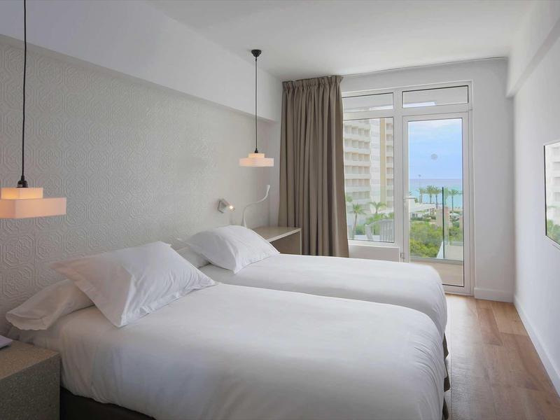 Jasny pokój hotelowy z dwoma pojedynczymi łóżkami i balkonem z widokiem na miasto.