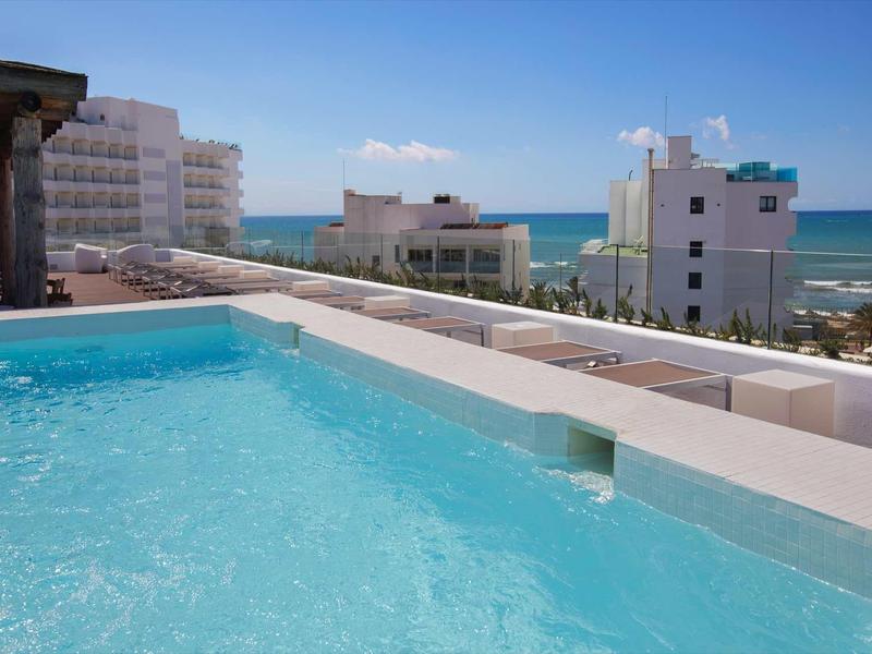 Widok z basenu hotelowego na morze i kilka budynków pod bezchmurnym niebem.