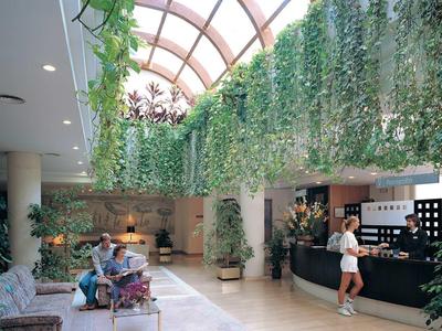 Hotel lobby with green glass roof and guests at the reception and on benches.