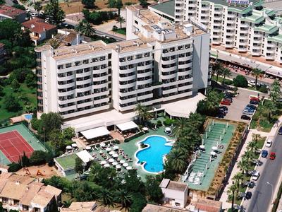 Hotel with pool, tennis courts, and surrounding buildings in an urban area.