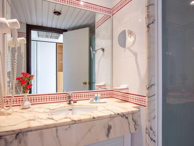Bright bathroom with large mirror, sink, and small vase with flowers decoration.