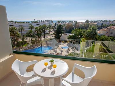 Balcony with small round table and two white chairs overlooking pool and city.
