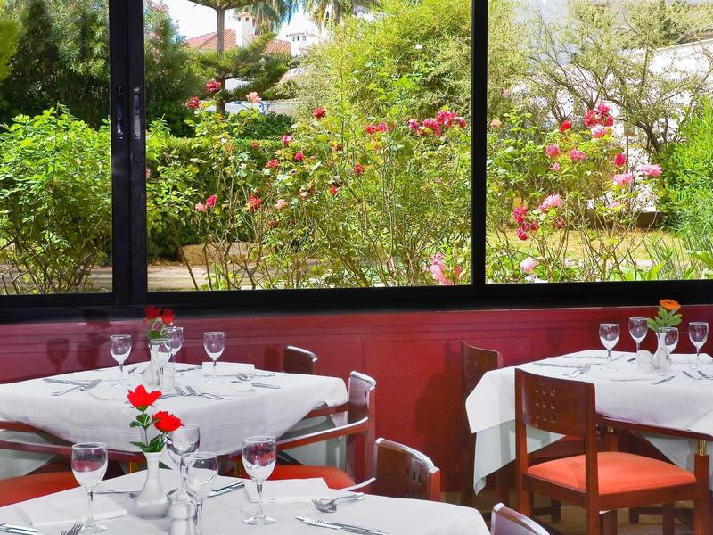 Restaurant with white tablecloths and a view of a green garden through large windows.