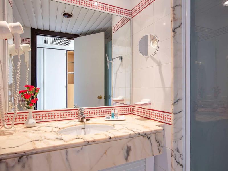 Bright bathroom with large mirror, sink, and small vase with flowers decoration.