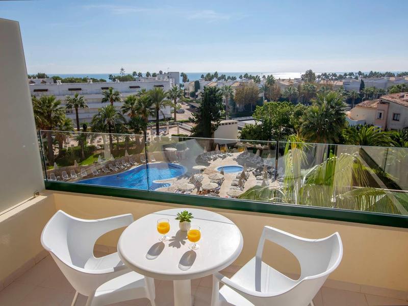 Balcony with small round table and two white chairs overlooking pool and city.