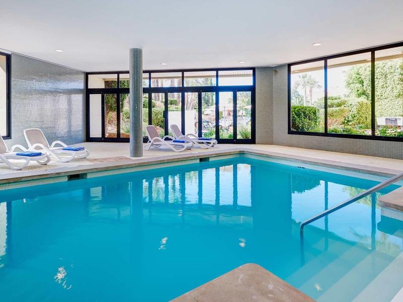 Indoor swimming pool with large windows and lounge chairs in a modern wellness area.