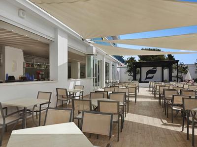 Venkovní terasa hotelu s množstvím stolů a židlí pod jasnou oblohou.