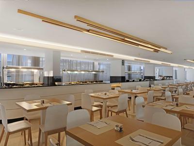 Nowoczesna hotelowa jadalnia z drewnianymi stołami i krzesłami, urządzona w neutralnych tonacjach.