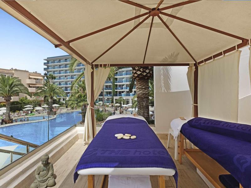 Dva masážní stoly pod slunečníkem vedle bazénu v moderním hotelu.