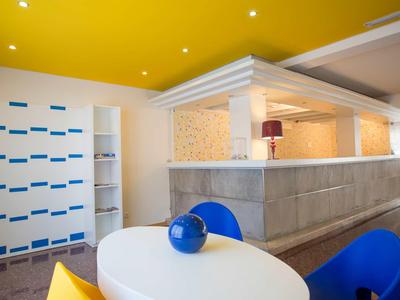 Área de lounge moderna de hotel con sillas coloridas, mesa blanca redonda y techo amarillo.