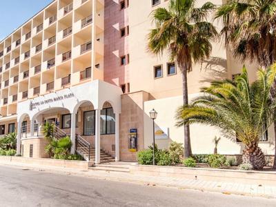 Multi-story hotel building with palm trees at the entrance on a sunny day.