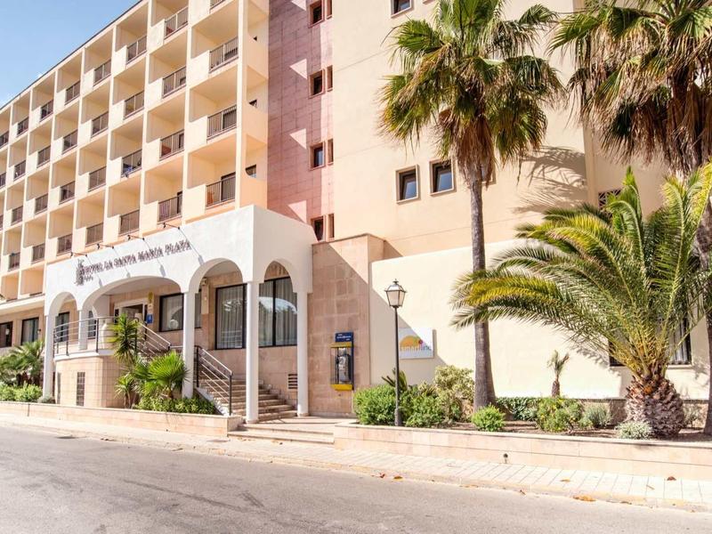 Multi-story hotel building with palm trees at the entrance on a sunny day.