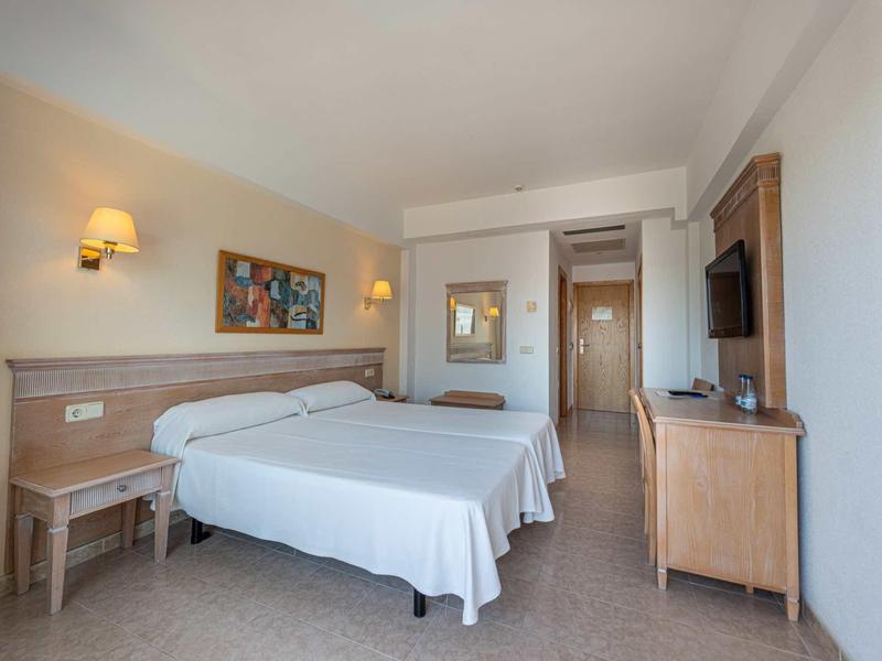 Bright hotel room with two single beds, desk, and wall-mounted TV.