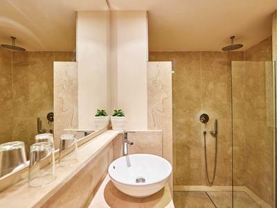 Modernes Badezimmer mit beige Fliesen, runder Waschtisch, Glasdusche und zwei kleinen grünen Pflanzen.