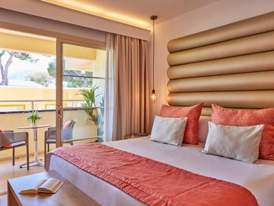 Helles Schlafzimmer mit großem Bett, roten Kissen, Balkon und Blick ins Freie.