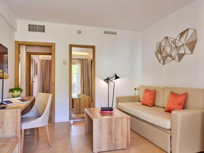 Helles Wohnzimmer mit beigem Sofa, orangen Kissen, Holzmöbeln und geometrischer Wanddekoration.