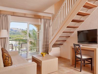 Helles Wohnzimmer mit Treppe, Sofa, Fernseher, Tisch und Balkon mit Bergblick.