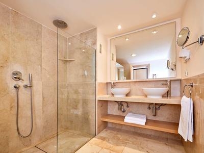 Modernes Badezimmer mit begehbarer Glasdusche, Doppelwaschbecken und großen Spiegeln.