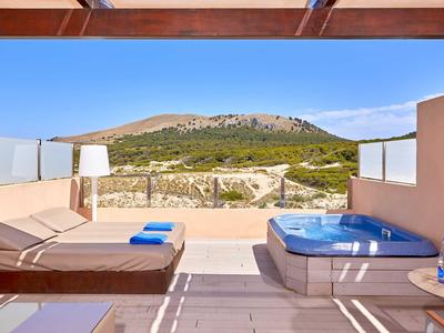 Terrasse mit Sonnenliegen und Whirlpool mit Blick auf Hügel und blauen Himmel.