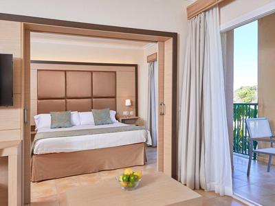 Modernes Hotelzimmer mit großem Bett, TV, Balkon und hellen, neutralen Farben.