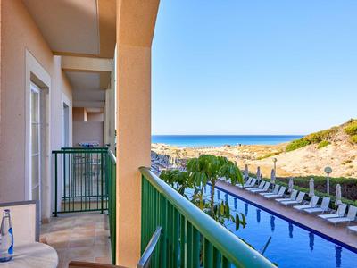 Balkon mit grünem Geländer, Blick auf Pool und Meer im Hintergrund bei klarem Himmel.