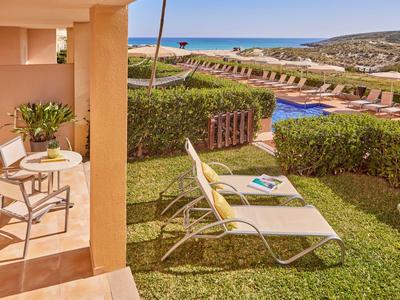 Balkon mit Stühlen, Liegestühlen und Blick auf Garten, Pool und Meer im Hintergrund.