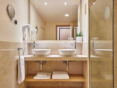 Helles Badezimmer mit Doppelwaschbecken, großer Spiegel, Handtüchern und begehbarer Dusche.