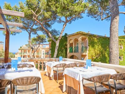 Terrassenrestaurant mit weißen Tischtüchern, blauen Servietten und vielen Bäumen im Sonnenschein.