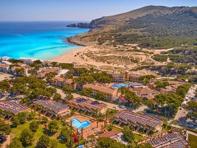 Blick auf eine Küstenlandschaft mit türkisfarbenem Meer, Sandstrand und Gebäuden im Grünen.