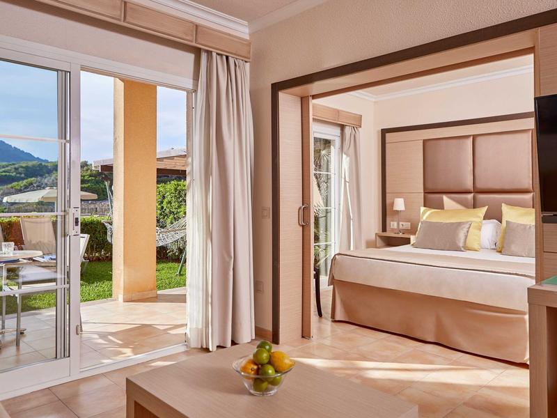 Moderní hotelový pokoj s terasou, posezením a výhledem na zelené kopce.