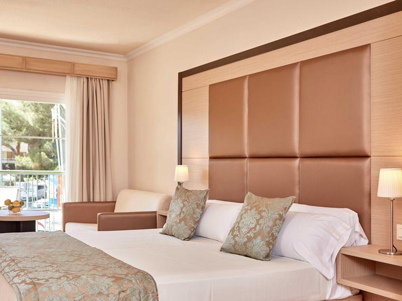 Hotelový pokoj se dvěma postelemi, polstrovaným čelem a posezením u velkého okna.