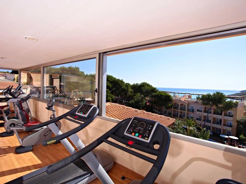 Posilovna s běžeckými pásy a velkými okny s výhledem na stromy a budovy.