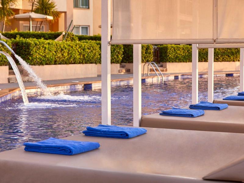 Bazénová oblast s lehátky a modrými ručníky v slunném hotelu.