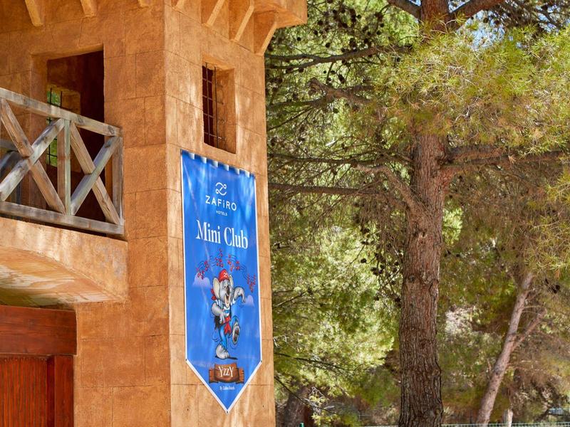 Venkovní prostor hotelu s dřevěným zábradlím a modrým uvítacím bannerem