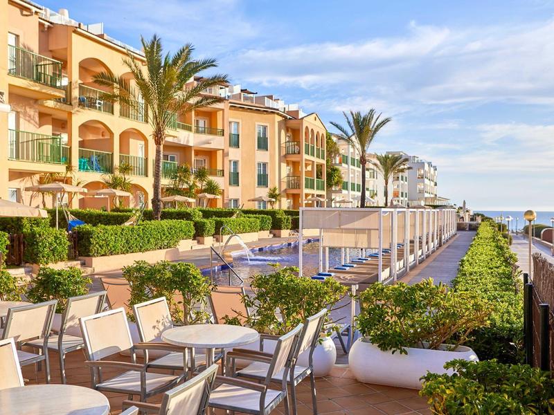 Hotelová terasa s stolky, židlemi a výhledem na moře za slunečného dne.