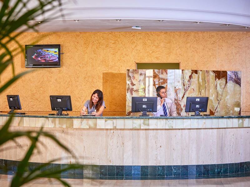 Recepce s dvěma zaměstnanci a třemi počítači v hotelu s moderním dekorací.