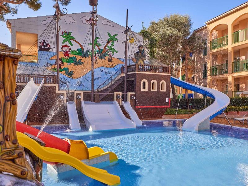 Barevné vodní skluzavky v bazénové oblasti s pirátskou lodí a posezením.
