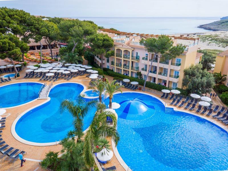 Velká hotelová bazénová oblast s několika bazény, lehátky a výhledem na moře.