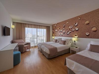 Habitación de hotel moderna con dos camas, zona de estar, televisor y balcón con vistas.