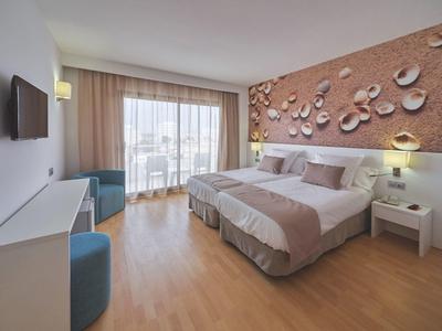 Habitación de hotel luminosa con dos camas individuales, ventana grande y suelo de madera.