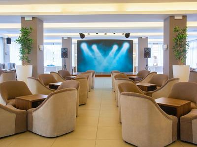 Área elegante de lounge en hotel con cómodos sillones y gran pantalla al fondo.