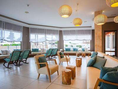 Amplia área de descanso con sillas y cojines frente a grandes ventanas, decorada con lámparas colgantes.