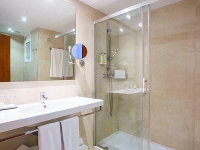 Baño moderno con ducha de vidrio, lavabo blanco y toallas, en tonos beige y luz cálida